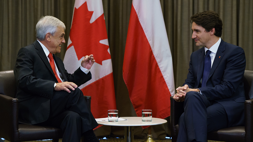 Prime Minister Justin Trudeau and President of Chile Sebastián Piñera sit and talk in an office beside flags representing Canada and Chile.