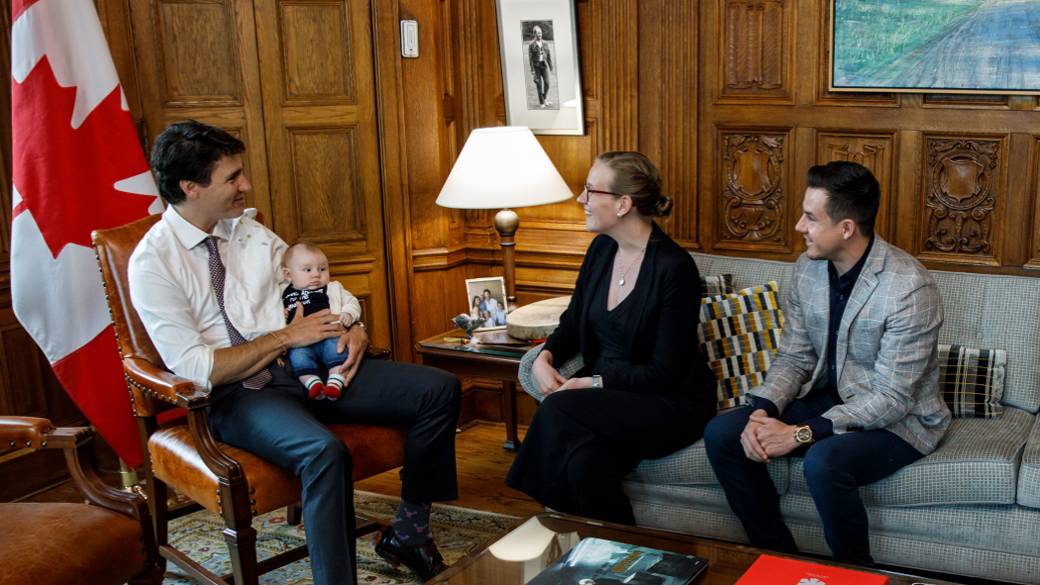 Prime Minister Justin Trudeau sits across from Minister Karina Gould and her partner Alberto Gerones holding their baby
