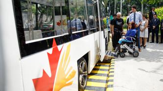 Le premier ministre Justin Trudeau et d’autres personnes regardent une femme en fauteuil roulant monter à bord du nouveau véhicule de transport en commun électronique Jeepney