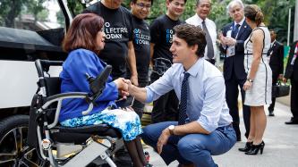 Prime Minister Justin Trudeau kneels down to eye level, shakes hands and speaks to a woman in a wheelchair while the Phillippino-Canadian innovators look on