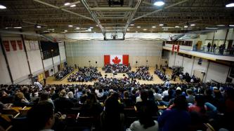 The audience is shown looking at the stage during a town hall discussion in a gymnasium.