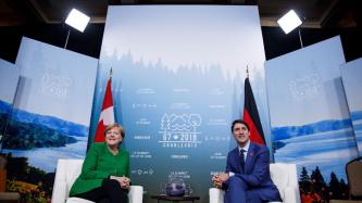 PM Trudeau and Chancellor Angela Merkel sit and look at the cameras.