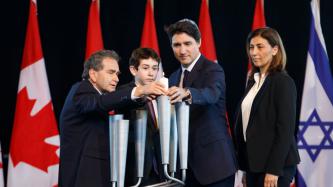 PM Trudeau, a man, and a boy place a candle in a holder