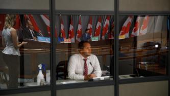 A man behind a window listens to PM Trudeau