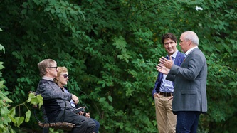 Les PMs Trudeau et Horgan discutent avec un couple assis sur un banc de parc