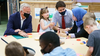 Le PM Trudeau regarde une femme assise à une table où des enfants jouent