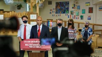 Le ministre Hussen à un lutrin avec les PM Trudeau et King et d’autres personnes à l’arrière