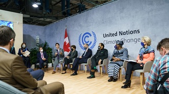 Le PM Justin Trudeau est assis avec d’autres personnes devant une grande bannière de l’ONU