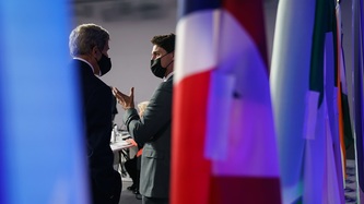 Le PM Justin Trudeau se tient près de drapeaux avec un homme à qui il fait des signes de la main