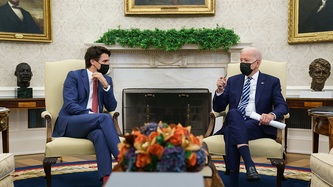 A fireplace behind them, President Biden motions with his hand as Prime Minister Trudeau looks on